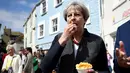 Perdana Menteri (PM) Inggris, Theresa May mencicipi beberapa keripik saat berhenti untuk kampanye di Mevagissey, Cornwall, Selasa (2/5). Theresa May melakukan kampanye dengan berkeliling jalanan di Cornwall. (Dylan Martinez/PA via AP)