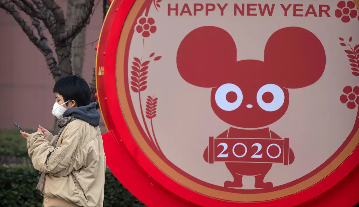Seorang perempuan mengenakan masker berdiri dekat layar untuk perayaan Imlek Tahun Tikus Logam di Beijing, 22 Januari 2020. Otoritas kesehatan China mendesak orang-orang menghindari keramaian dan pertemuan publik di Wuhan, kota yang menjadi pusat penyebaran wabah virus corona. (AP/Mark Schiefelbein)