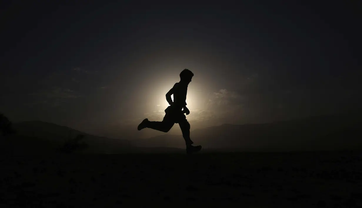 Seorang bocah Afganistan bermain saat matahari terbenam di puncak bukit di pinggiran Kabul, Afghanistan pada 25 Juli 2020. (AP Photo / Rahmat Gul)