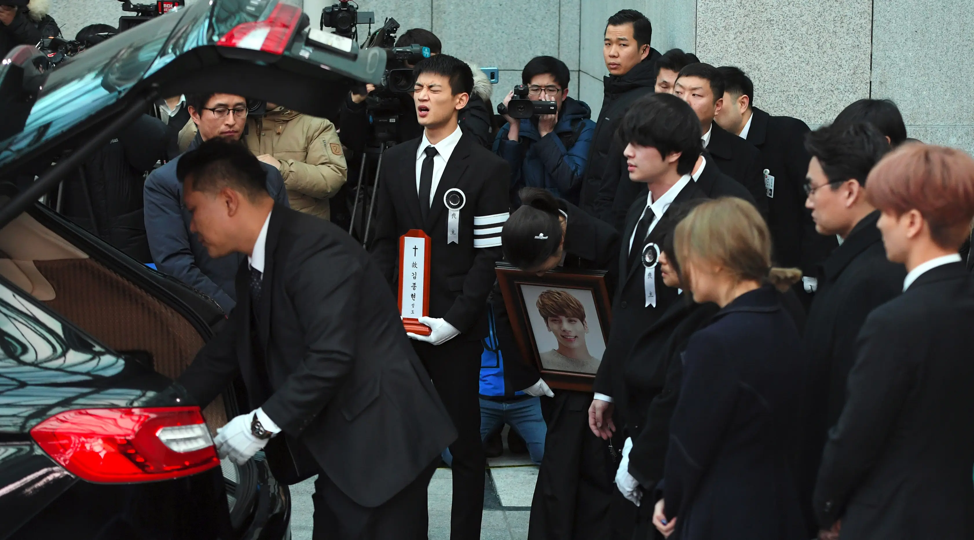 Choi Minho (membawa plakat) berusaha menahan kesedihan saat peti jenazah sang sahabat, Jonghyun SHINee dimasukkan ke mobil menuju tempat pemakaman dari rumah persemayaman di Asan Hospital, Seoul, Kamis (21/12). (JUNG Yeon-Je/AFP)