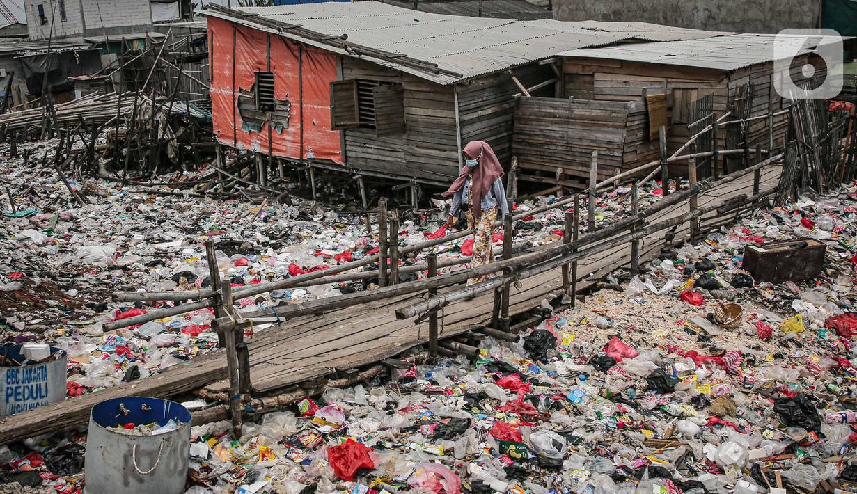 Warga berjalan di jembatan kayu di antara sampah di perkampungan nelayan Cilincing, Jakarta, Minggu (21/2/2022). Peringatan HPSN 2022, Pemprov DKI Jakarta mengajak warga Jakarta peduli sampah mulai dari lingkungan terdekat dengan cara memilah sampah dari rumah. (Liputan6.com/Faizal Fanani)
