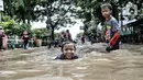 Anak-anak bermain air saat banjir menggenangi Jalan Jatinegara Barat, Jakarta, Senin (8/2/2021). Ketinggian air yang menggenangi Jalan Jatinegara Barat mencapai setinggi paha orang dewasa, sehingga menyebabkan kemacetan. (merdeka.com/Iqbal S. Nugroho)