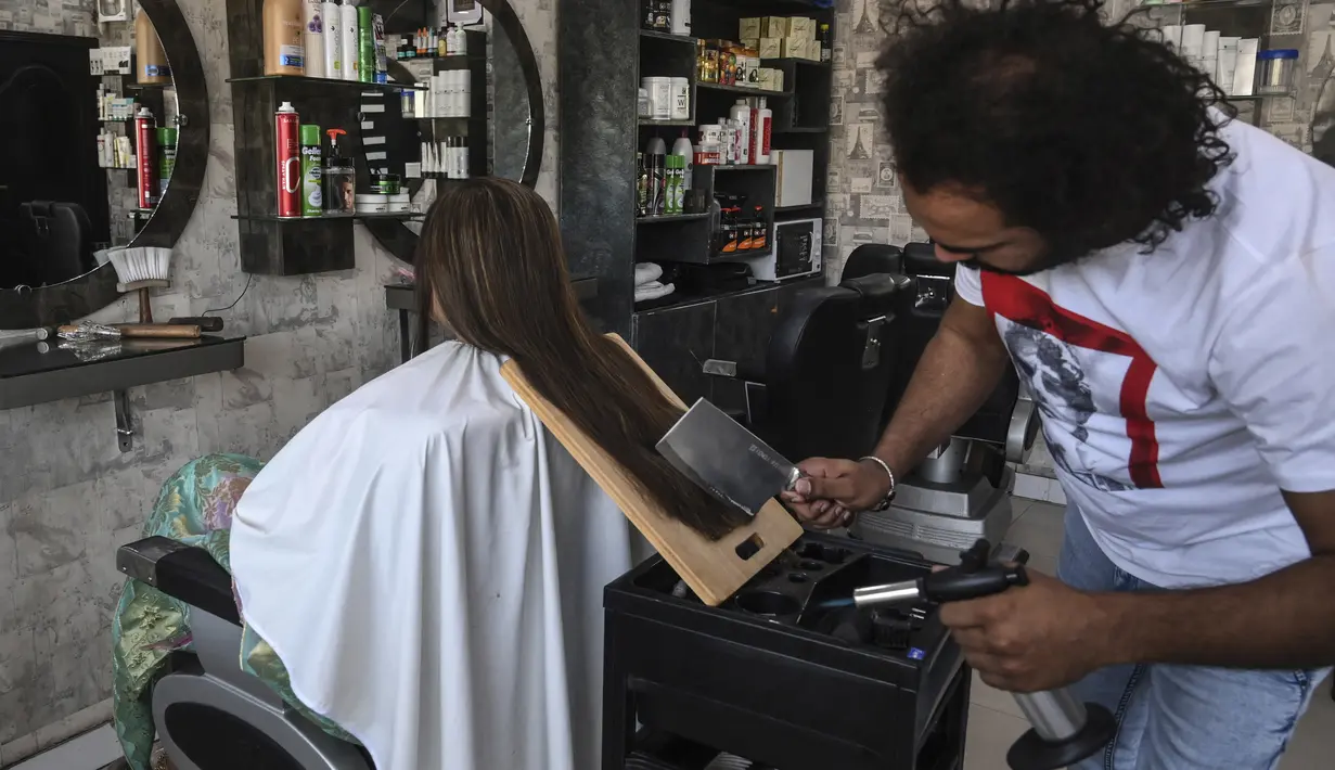 Dalam gambar pada 8 April 2021, tukang cukur Pakistan Ali Abbas menggunakan pisau daging untuk memotong rambut seorang pelanggan di tokonya di Lahore. Berharap membuktikan kemampuannya dalam persaingan, Ali Abbas mengandalkan berbagai alat yang tidak biasa untuk melatih keahliannya. (Arif ALI/AFP)