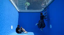 Pengunjung berfoto di karya seni Swimming Pool dalam sebuah pameran di Museum CAFA, Beijing, 23 Juli 2019. Bagian atas karya seni unik itu berlapis kaca transparan yang dilapisi air sedalam 10 cm, sedangkan bagian bawahnya merupakan ruang kosong dengan dinding berwarna biru muda. (WANG Zhao/AFP)
