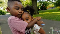 Zavion Guzman memeluk saudara perempuannya, Jazzmyn saat bermain di Belleville, New Jersey pada 30 Juni 2021. Lunisol Guzman mengadopsi keduanya saat masih bayi tetapi meninggal tahun lalu karena COVID-19 bersama pasangannya di awal gelombang pertama pandemi. (AP Photo/Mary Altaffer)