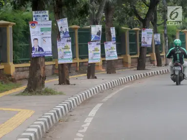 Pengemudi ojek online melintas dekat Alat Peraga Kampanye (APK) yang dipasang di pohon kawasan Ciater, Tangerang selatan, Senin (1/4). Pemasangan APK sejumlah caleg yang dipaku di pohon melanggar peratuan KPU Nomor 15 Tahun 2013 tentang tata cara pemasangan APK. (merdeka.com/Arie Basuki)