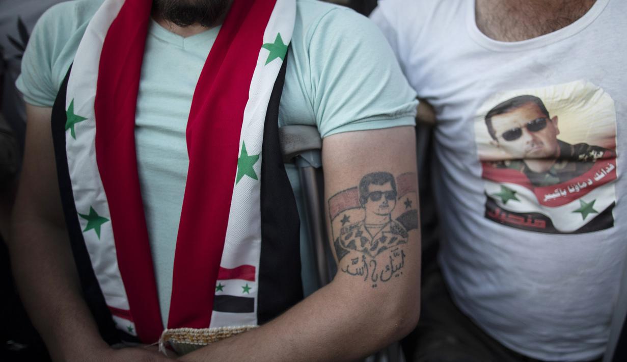 Seorang tentara Suriah yang terluka dengan tato Presiden Bashar Assad saat mereka merayakan kemenangannya di Omayyad Square, di Damaskus, Kamis (27/5/2021). Bashar al-Assad terpilih kembali untuk masa jabatan keempat sebagai presiden Suriah yang dilanda perang. (AP Photo/Hassan Ammar)