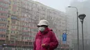 Seorang perempuan yang mengenakan masker berjalan di sepanjang jalan yang berkabut dan tercemar di Beijing, Sabtu (6/11/2021). Jalan raya dan taman bermain sekolah di Beijing ditutup pada Jumat (5/11) karena polusi kabut asap yang tebal, setelah China meningkatkan produksi batu bara. (JADE GAO/AFP)