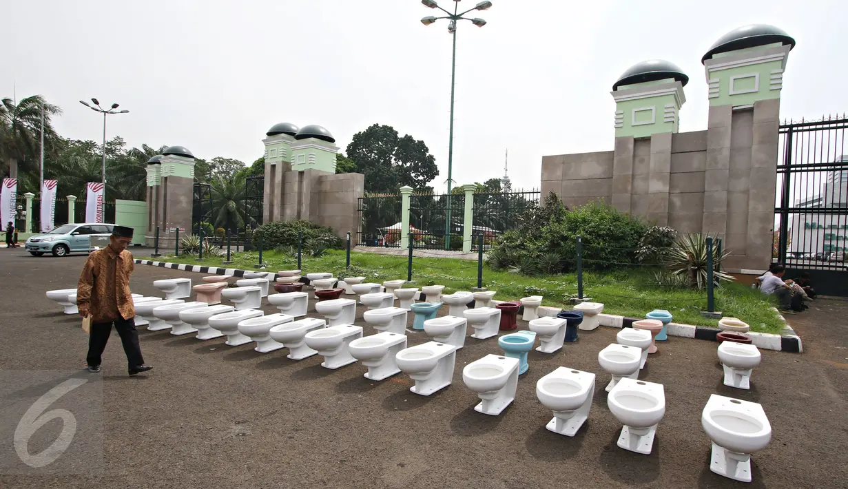 Seorang pria melintas di depan puluhan jamban yang di letakkan di depan gedung DPR RI, Jakarta, Kamis (3/12). Aksi yang dinamakan “Aksi Djamban DPR” ini menyindir kasus “Papa Minta Saham” yang dilakukan Setya Novanto. (Liputan6.com/Immanuel Antonius)