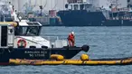 Seorang pekerja pembersihan di atas kapal berdiri di atas alat penyedot minyak selama operasi untuk membersihkan minyak dari tumpahan minyak di dekat terminal pelabuhan Pasir Panjang di Singapura pada tanggal 18 Juni 2024. (ROSLAN RAHMAN/AFP)