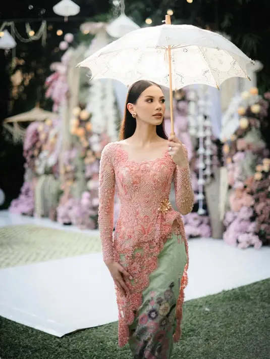 Alyssa Daguise tampil bak calon pengantin modern dalam balutan kebaya pink lembut penuh detail payet dan bordir floral. Siluet kebaya yang fitted mempertegas bentuk tubuhnya, sementara kain bawahan warna pastel dengan motif bunga memberi kesan manis dan romantis.  [@alyssa.daguise].