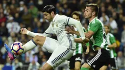 Penyerang Real Madrid, Alvaro Morata, menghindari gelandang Real Betis, Alin Tosca. Bermain di kandang, anak asuhan Zinedine Zidane lebih menguasai jalannya laga dengan penguasaan bola 62 persen. (AFP/Gerard Julien)