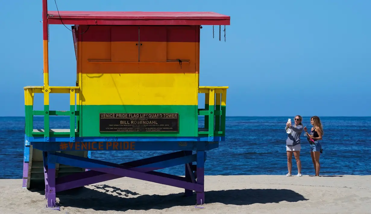 Dua wanita berselfie di dekat menara penjaga pantai Venice Pride Flag di daerah Venice Beach, Los Angeles (13/5/2020). Los Angeles County membuka kembali pantai-pantainya pada Rabu dalam pelonggaran terbaru pembatasan coronavirus. (AP/Mark J. Terrill)
