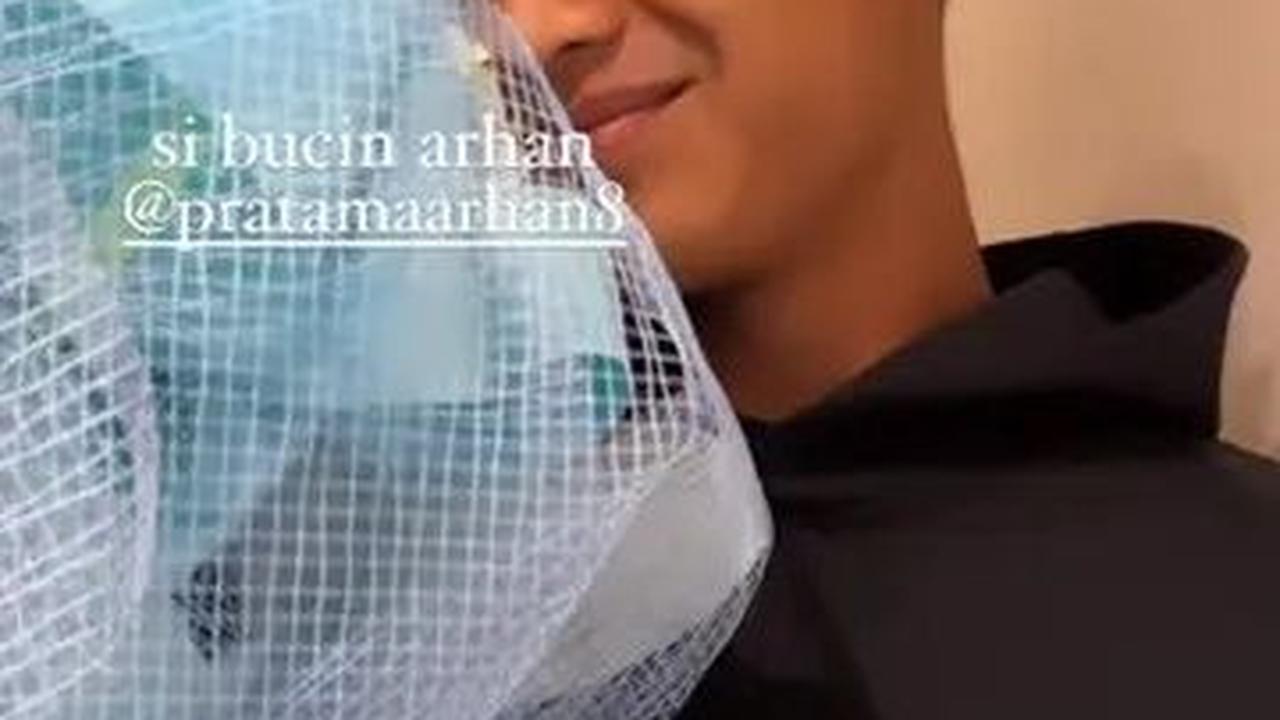 Arhan berdiri di depan pintu kamar dengan membawa sebuah keranjang bunga biru dan kue tart yang bertuliskan 'Selamat Ulang Tahun, Istriku'.