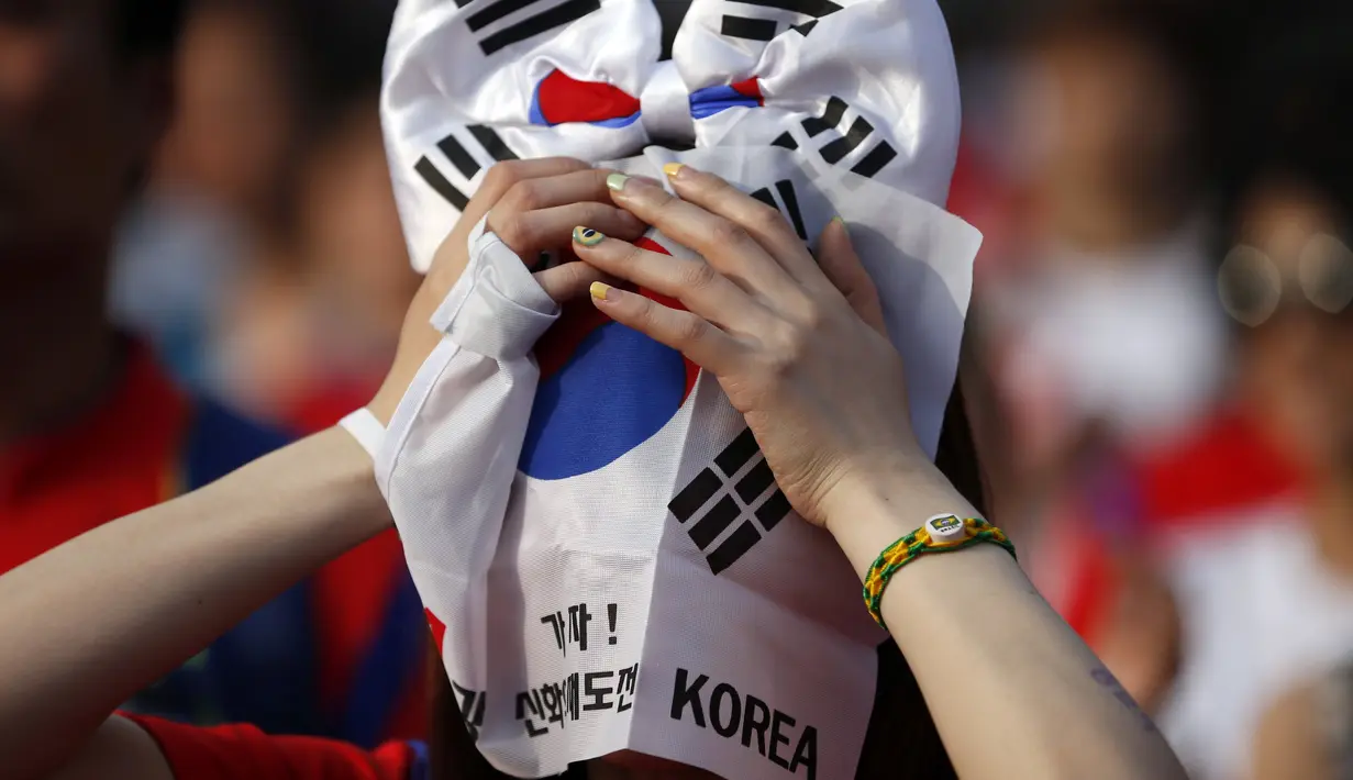Seorang warga menutupi wajahnya dengan bendera Korea Selatan usai timnasnya dikalahkan Belgia 0-1, Seoul, Jumat (27/6/14). (REUTERS/Kim Hong-Ji)