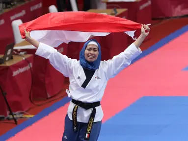Atlet Taekwondo putri Indonesia, Defia Rosmaniar mengibarkan bendera Merah Putih saat merayakan kemenangan atas Salahshouri Marjan (Iran) pada Final Women Individual Poomsae di JCC, Jakarta, Minggu (19/8). (Liputan6.com/Helmi Fithriansyah)