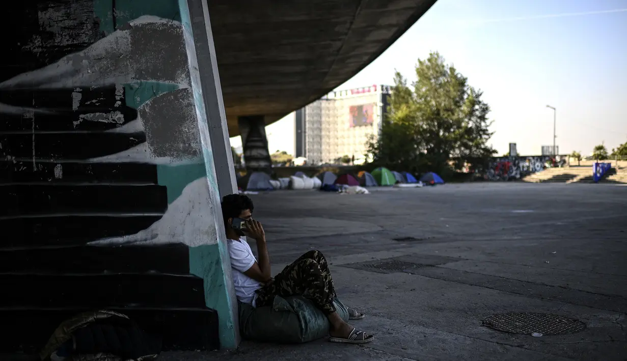 Seorang pencari suaka Afghanistan melakukan panggilan telepon di kamp migran darurat yang terletak di bawah jalan raya A1 di utara pinggiran kota populer Paris Saint-Denis (16/9/2020). (AFP/Christophe Archambault)