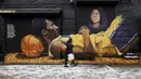 Seorang warga melintas di depan lukisan mural bintang LA Lakers, Kobe Bryant dan putrinya, Gianna di New York City, Selasa (26/1/2021). Lukisan dibuat untuk mengenang 1 tahun tragedi kecelakaan helikopter yang menewaskan keduanya. (Getty Images via AFP/Sarah Stier)