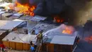 Warga membantu petugas pemadam kebakaran memadamkan api di lingkungan berpenghasilan rendah Laguna Verde, di Iquique, Chile, Senin (10/1/2022). Menurut pihak berwenang, api menghanguskan hampir 100 rumah di lingkungan itu yang sebagian besar dihuni oleh para migran. (AP Photo/Ignacio Munoz)