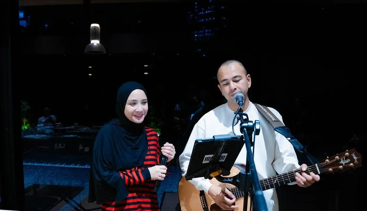 Nagita Slavina tampil bernyanyi bersama sang suami Raffi Ahmad. Ia mengenakan atasan lengan panjang bercorak garis merah hitam, dipadunya dengan celana panjang dan hijab hitam polos. [Foto: Instagram/raffinagita1717]
