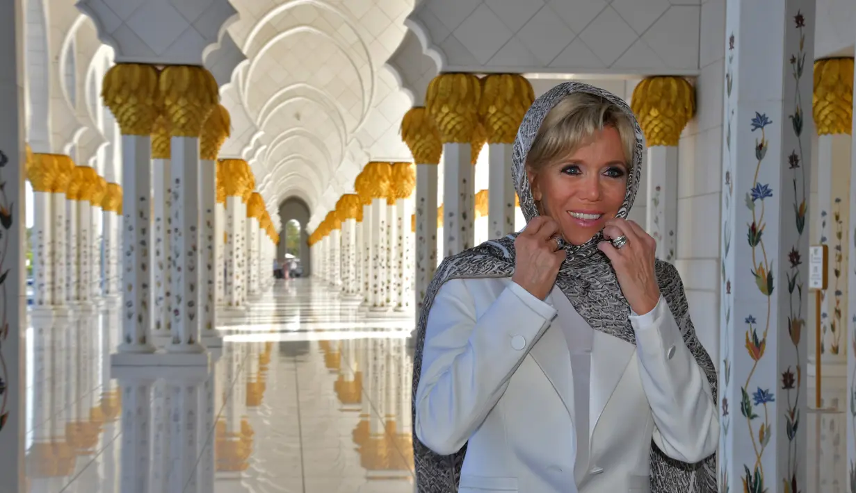 Istri Presiden Prancis, Brigitte Macron merapikan penutup kepalanya saat mengunjungi Masjid Sheik Zayed di Abu Dhabi, Kamis (9/11). Di masjid itu, Brigitte terlihat mengenakan penutup kepala bermotif leopard dan melepas sepatu. (Giuseppe CACACE / AFP)