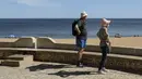 Sepasang turis melihat pantai di Albufeira, wilayah Algarve, Portugal, Senin (17/5/2021). Wisatawan Inggris mulai berdatangan dalam jumlah besar di bagian selatan Portugal pada hari Senin, setelah pemerintah di kedua negara melonggarkan pembatasan perjalanan pandemi COVID-19. (AP Photo/Ana Brigida)