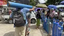 Seorang pria membawa tangki oksigen sementara yang lain berbaris untuk mengantre di luar stasiun pengisian ulang oksigen di kota Pazundaung di Yangon, Minggu (11/7/2021). Myanmar mengalami lonjakan kasus COVID-19, memicu kelangkaan pasokan oksigen yang sangat dibutuhkan pasien. (AP Photo)