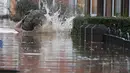 Warga tersandung saat melintasi banjir yang merendam jalan pemukiman di Carlisle, Inggris, Minggu (6/12). Puluhan ribu rumah tidak punya listrik karena Badai Desmond yang menyebabkan banjir di Inggris utara dan sebagian Skotlandia. (REUTERS/Phil Noble)