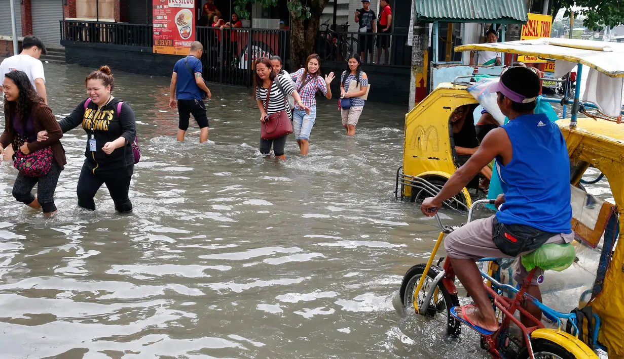 Warga berjalan di antara banjir yang terjadi di Metropolitan Manila, Filipina, Jumat (20/7). Banjir diakibatkan hujan musim angin barat daya yang dibawa oleh badai tropis. (AP Phoyo/Aaron Favila)
