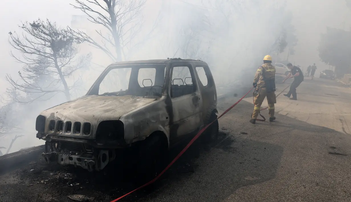 Seorang petugas pemadam kebakaran dan polisi beroperasi selama kebakaran hutan di pinggiran Voula, di selatan Athena, Yunani, Sabtu, 4 Juni 2022. Kombinasi cuaca panas, kering, dan angin kencang membuat Yunani rentan terhadap wabah kebakaran hutan setiap musim panas. (AP Photo/Yorgos Karahalis)