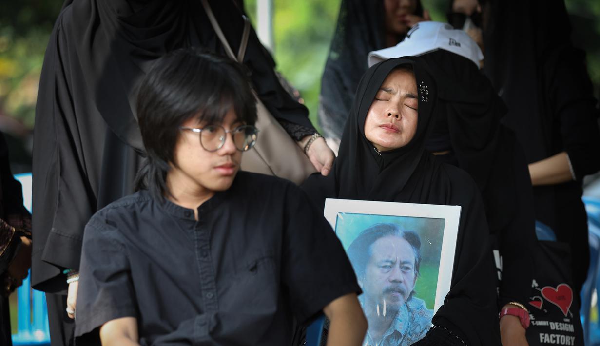 Tubuhnya yang tak berdaya, terus mendekap erat foto suami di sepanjang perjalanan menuju liang lahad. Tampak dalam foto, Karina Ranau (kanan) sesaat sebelum pemakaman suaminya, Epy Kusnandar, di Tempat Pemakaman Umum (TPU) Jeruk Purut, Jakarta Selatan, Kamis (4/12/2025) pagi. (Kapanlagi.com/Budy Santoso)