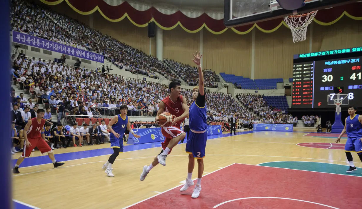 Pemain Korea Utara (merah) berusaha melewati pemain Korea Selatan (biru) selama pertandingan basket pria di Stadion Indoor Ryugyong Chung Ju-Yung, Pyongyang (5/7). Tim pria Korea Utara memenangkan 82-70. (AFP Photo/Kim Won-Jin)