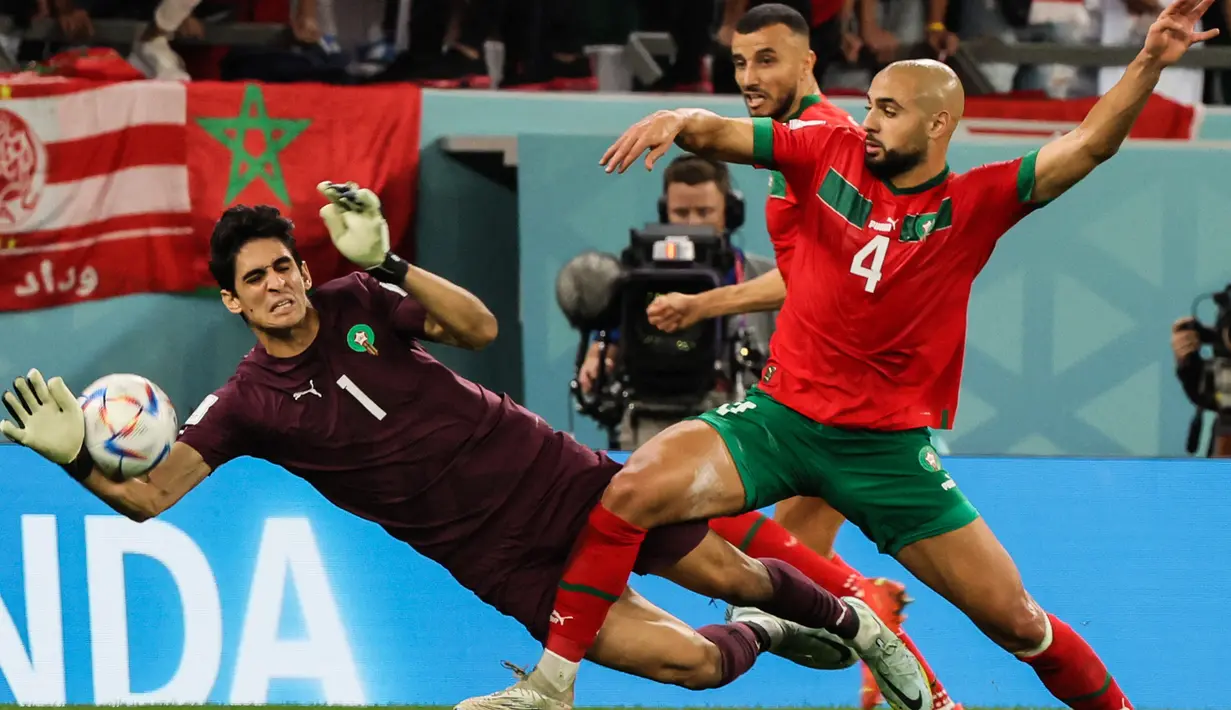 Kiper Maroko #01 Yassine Bounou dan gelandang Maroko #04 Sofyan Amrabat berusaha meraih bola pada babak 16 besar Piala Dunia 2022 menghadapi Spanyol di Education City Stadium, Al Rayyan, Rabu (6/12/2022) dini hari WIB. Hakim Ziyech dkk. menang dramatis di babak adu penalti. (JACK GUEZ / AFP)