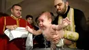 Ekspresi seorang bayi saat pendeta mengangkatnya dari air dalam acara pembaptisan massal di Gereja Katedral Holy Trinity, Tbilisi, Georgia (21/1). (AFP Photo/Vano Shlamov)