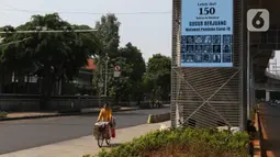 Pedagang melintasi videotron penghormatan kepada tenaga medis yang gugur akibat Covid-19 di tiang penyangga lintasan MRT, Jalan Sisingamangaraja, Jakarta, Jumat (18/9/2020). Keberadaan videotron tersebut diharap mampu membuat masyarakat waspada akan ancaman Covid-19. (Liputan6.com/Herman Zakharia)