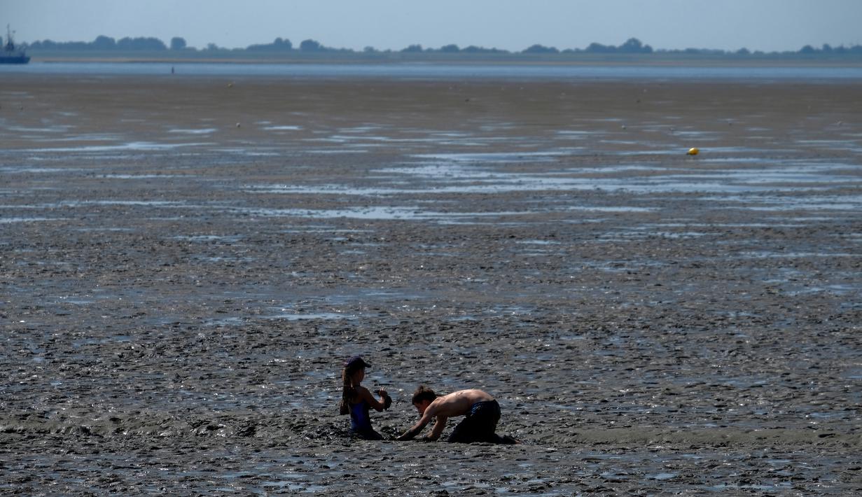 Anak-anak bermain lumpur saat suhu mencapai 34 derajat Celcius di dekat pantai Laut Utara di Wremen, Jerman barat (24/7/2019). Peramal cuaca memprediksi suhu tertinggi di seluruh Eropa barat yang terkena gelombang panas akan mencetak rekor suhu terbaru.  (AFP Photo/Patrik Stollarz)