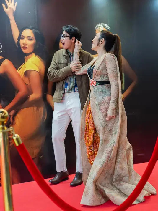 Gisel mengenakan outerwear panjang bermotif floral yang menjuntai dramatis, dipadukan dengan bustier hitam dan bawahan wastra bernuansa merah keemasan.  [@cintabrian].