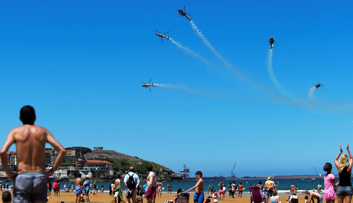 Tim aerobatik Patrulla Aspa bermanuver menggunakan helikopter saat menghebohkan pengunjung pantai di atas Pantai San Lorenzo di Gijon, Spanyol, Minggu (24/7). (REUTERS/Eloy Alonso)