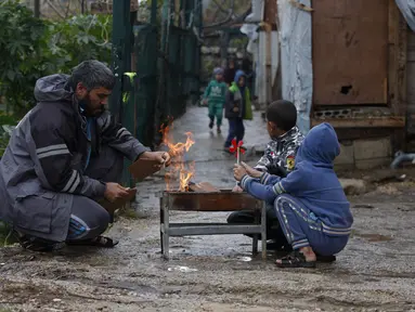 Sebuah keluarga pengungsi Suriah menghangatkan diri di sekitar api di sebuah kamp pengungsi di kota pelabuhan selatan Sidon, Lebanon pada 19 Januari 2022. Badai salju di Timur Tengah telah membuat banyak warga Lebanon dan Suriah berebut mencari cara untuk bertahan hidup. (AP Photo/Mohammed Zaatari)