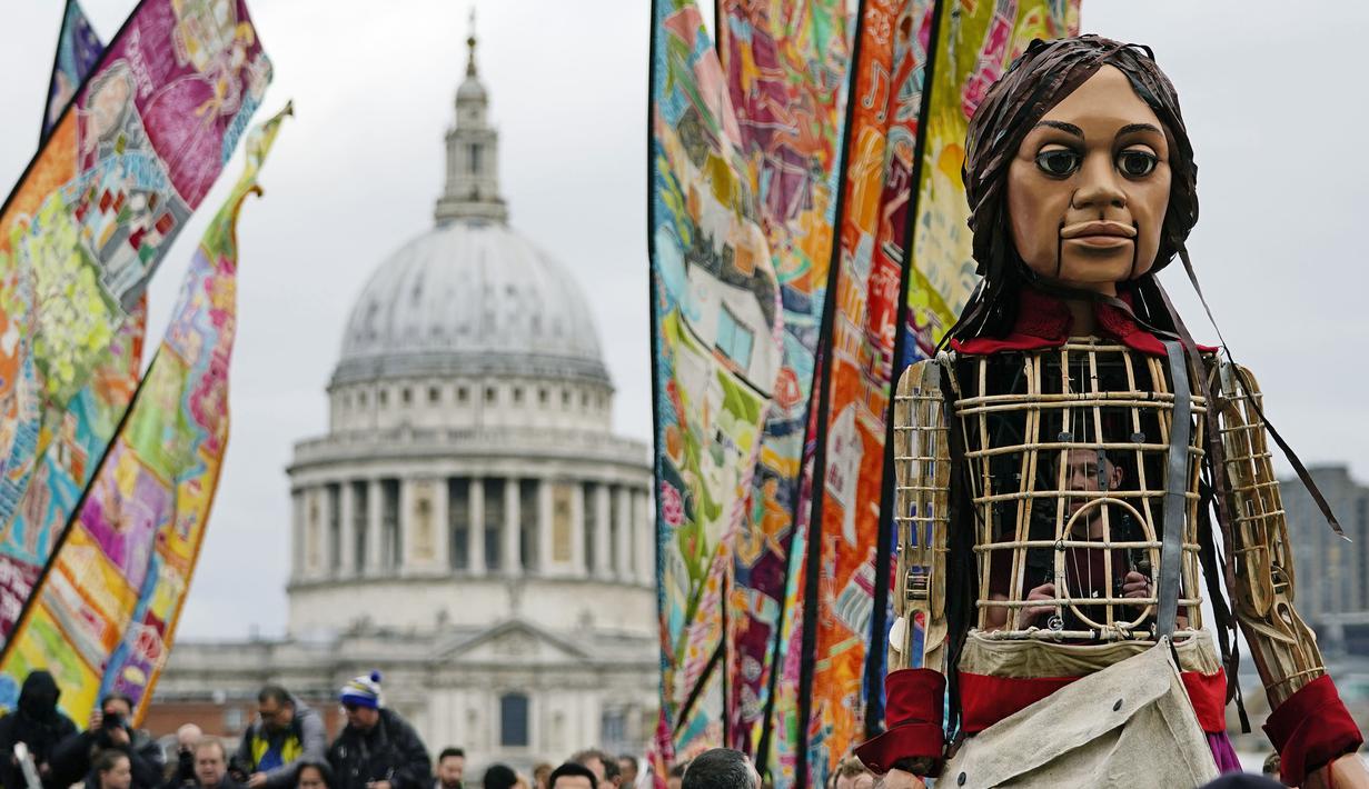 Boneka raksasa Little Amal saat tiba di kota London, Inggris, Sabtu (23/10/2021). Boneka Little Amalmenggambarkan perjalanan seorang pengungsi anak dari Suriah yang harus menempuh perjalanan ribuan kilometer demi memulai kehidupan baru dari negara asalnya. (Aaron Chown/PA via AP)