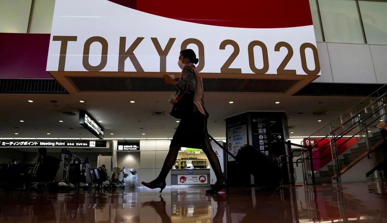 Seorang pramugari berjalan di depan layar besar Olimpiade Tokyo 2020 di Bandara Internasional Narita, Tokyo, Kamis (15/7/2021). Upacara pembukaan Olimpiade Tokyo akan digelar pada 23 Juli 2021 dan berakhir pada 8 Agustus 2021. (AP Photo/Kiichiro Sato)