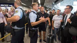 Petugas kepolisian memberi penjelasan kepada calon penumpang di aula terminal 1 Bandara Frankfurt, Jerman, Selasa (7/8). Sejumlah penerbangan harus dibatalkan setelah seorang yang tak dikenal menyusup melewati pos pemeriksaan. (Boris Roessler/dpa via AP)