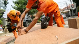 Petugas PPSU memproduksi peti jenazah di halaman Kantor Kelurahan Kayu Putih, Jakarta, Selasa, (6/7/2021). Kelurahan Kayu Putih berinisiatif membuat peti jenazah dilatar belakangi warganya yang terkendala ketersediaan peti saat angka kematian COVID-19 meningkat di DKI. (Liputan6.com/Faizal Fanani)