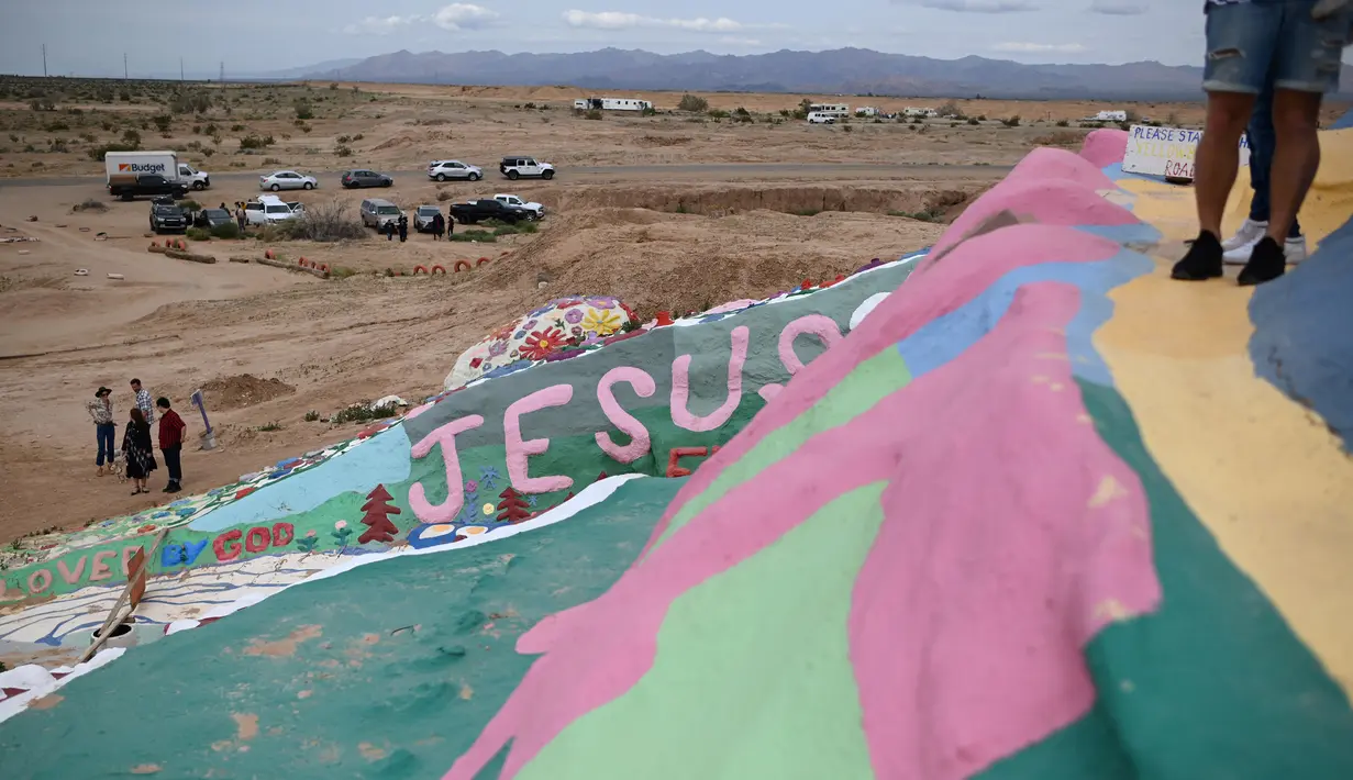 Turis mengunjungi Salvation Mountain, sebuah lereng bukti di Niland, California, Amerika Serikat. Dibangun dari kumpulan jerami, dempul jendela dan lebih dari 10,000 galon cat yang dipergunakan untuk membuat bukit tetap berdiri, dan melindunginya dari pasir dan angin gurun. (Robyn Beck/AFP)