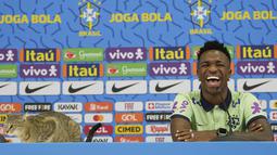 Penyerang Brasil Vinicius Junior tersenyum saat seekor kucing duduk di atas meja selama konferensi pers jelang Kroasia vs Brasil pada perempat final Piala Dunia 2022, di Stadion Al Arabi SC di Doha, Rabu (7/12/2022). Kucing dengan perpaduan warna coklat dan hitam itu langsung naik ke atas meja. (AP Photo/Andre Penner)