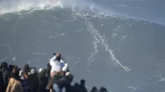 Orang-orang menyaksikan peselancar menaiki ombak saat sesi selancar ombak besar di Praia do Norte atau Pantai Utara, di Nazare, Portugal, (8/1/2022). Setiap tahunnya peselancar profesional menantang adrenalinnya mengarungi ombak besar dan tinggi di Pantai Praia do Norte. (AP Photo/Armando Franca)