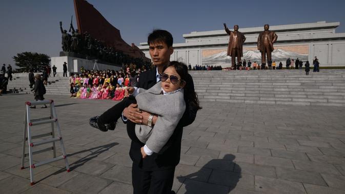 Seorang lelaki membawa seorang anak setelah mengunjungi kompleks Bukit Mansu di Pyongyang (AFP)