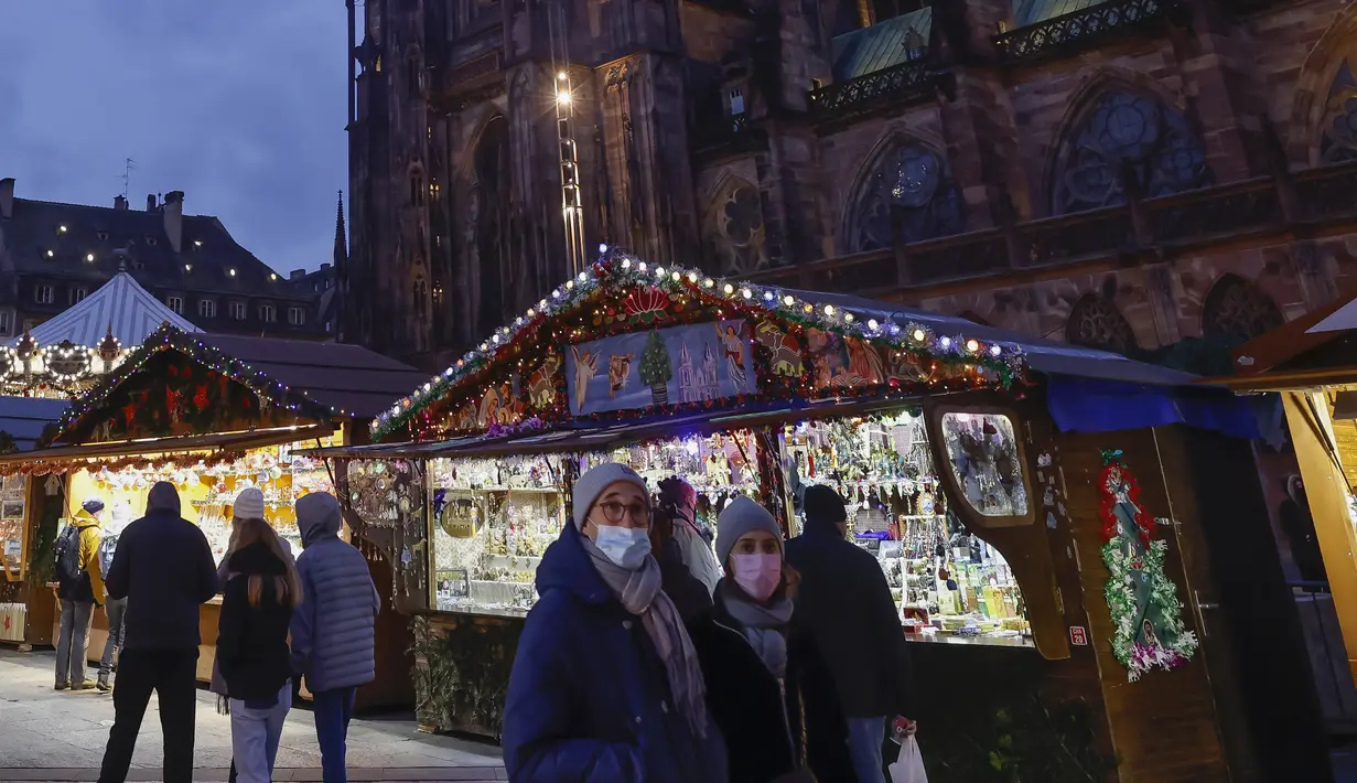 Pembeli yang mengenakan masker berjalan-jalan di pasar Natal di Strasbourg, Prancis, Jumat (26/11/2021). Prancis mengumumkan keputusan suntikan Booster Covid-19 untuk semua orang dewasa agar tak lagi menerapkan pembatasan wilayah, atau batasan jam malam. (AP Photo/Jean-Francois Badias)