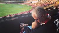 Perdana Menteri Australia, Malcom Turnbull, menonton pertandingan football sambil momong cucu dan membawa bir. (Foto: Facebook Malcolm Turnbull)