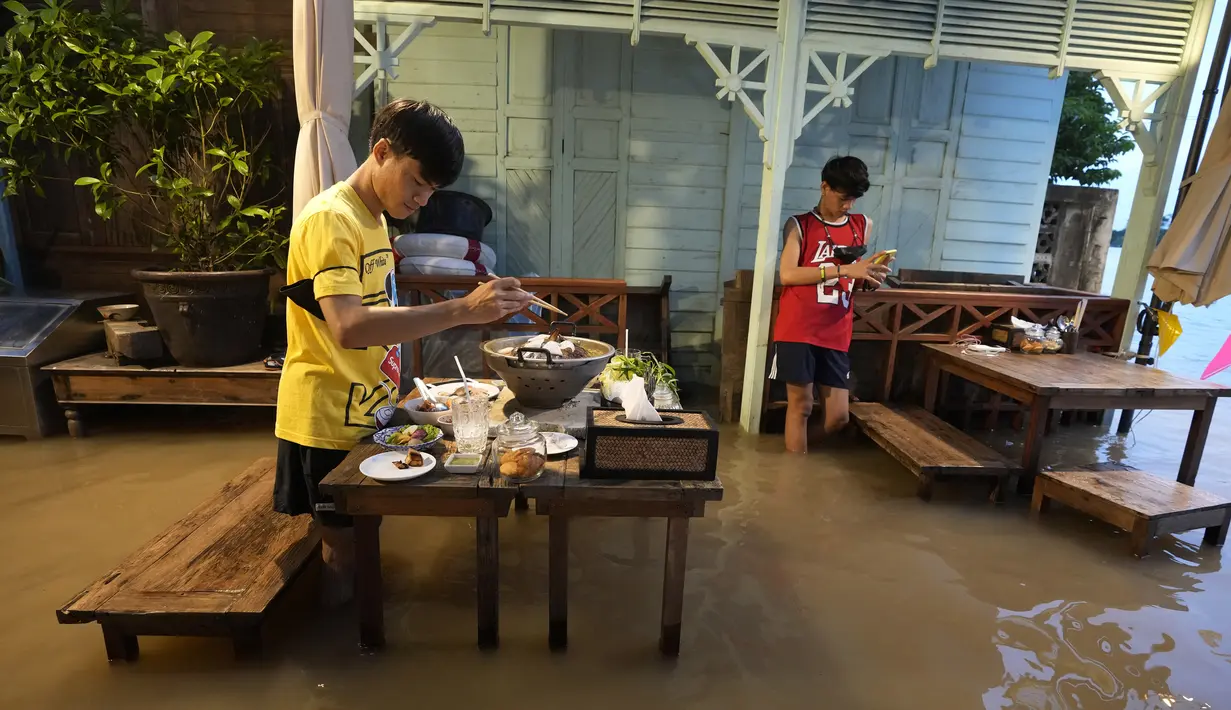 Pelanggan Chaopraya Antique Café di tepi sungai menikmati ketinggian air di Sungai Chao Phraya dekat Bangkok, Thailand, Kamis (7/10/2021). Restoran yang dilanda banjir ini menjadi tempat makan tidak biasa di mana pengunjung menikmati santapan makanan dengan kaki terendam. (AP Photo/Sakchai Lalit)